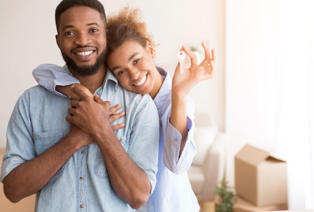 Cheerful Black Couple Holding New Home Key Hugging Standing In Own House After Relocation